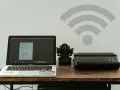 Laptop z projektem graficznym i drukarka obok figurki Ganesha. Symbol Wi-Fi nad nimi sugeruje bezprzewodowe drukowanie.