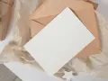 Brązowa koperta z białą kartką i ozdobnym nadrukiem na kopercie.
