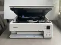 Biała drukarka Canon z otwartą pokrywą, widoczne tusze. Poradnik jak zainstalować drukarkę Canon.