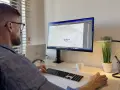 Mężczyzna pracuje przy komputerze, projektując logo na koszulkę. Pokazuje, jak napisać tekst na komputerze i go wydrukować.