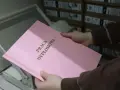 Różowa okładka z napisem "PRACA DYPLOMOWA" w złotych literach, trzymana w dłoniach nad bindownicą.