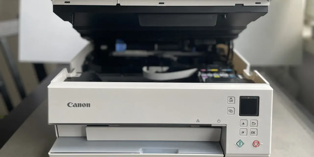 Biała drukarka Canon z otwartą pokrywą, widoczne tusze. Poradnik jak zainstalować drukarkę Canon.