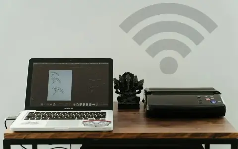 Laptop z projektem graficznym i drukarka obok figurki Ganesha. Symbol Wi-Fi nad nimi sugeruje bezprzewodowe drukowanie.