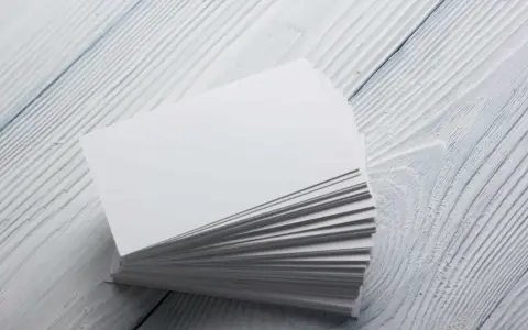 Stos białych wizytówek, idealnych na papier satynowy lub kredowy, leży na drewnianym blacie.