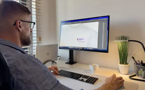 Mężczyzna pracuje przy komputerze, projektując logo na koszulkę. Pokazuje, jak napisać tekst na komputerze i go wydrukować.