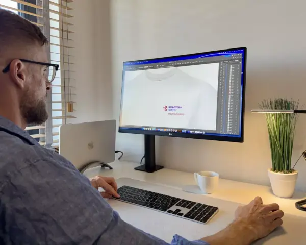Mężczyzna pracuje przy komputerze, projektując logo na koszulkę. Pokazuje, jak napisać tekst na komputerze i go wydrukować.