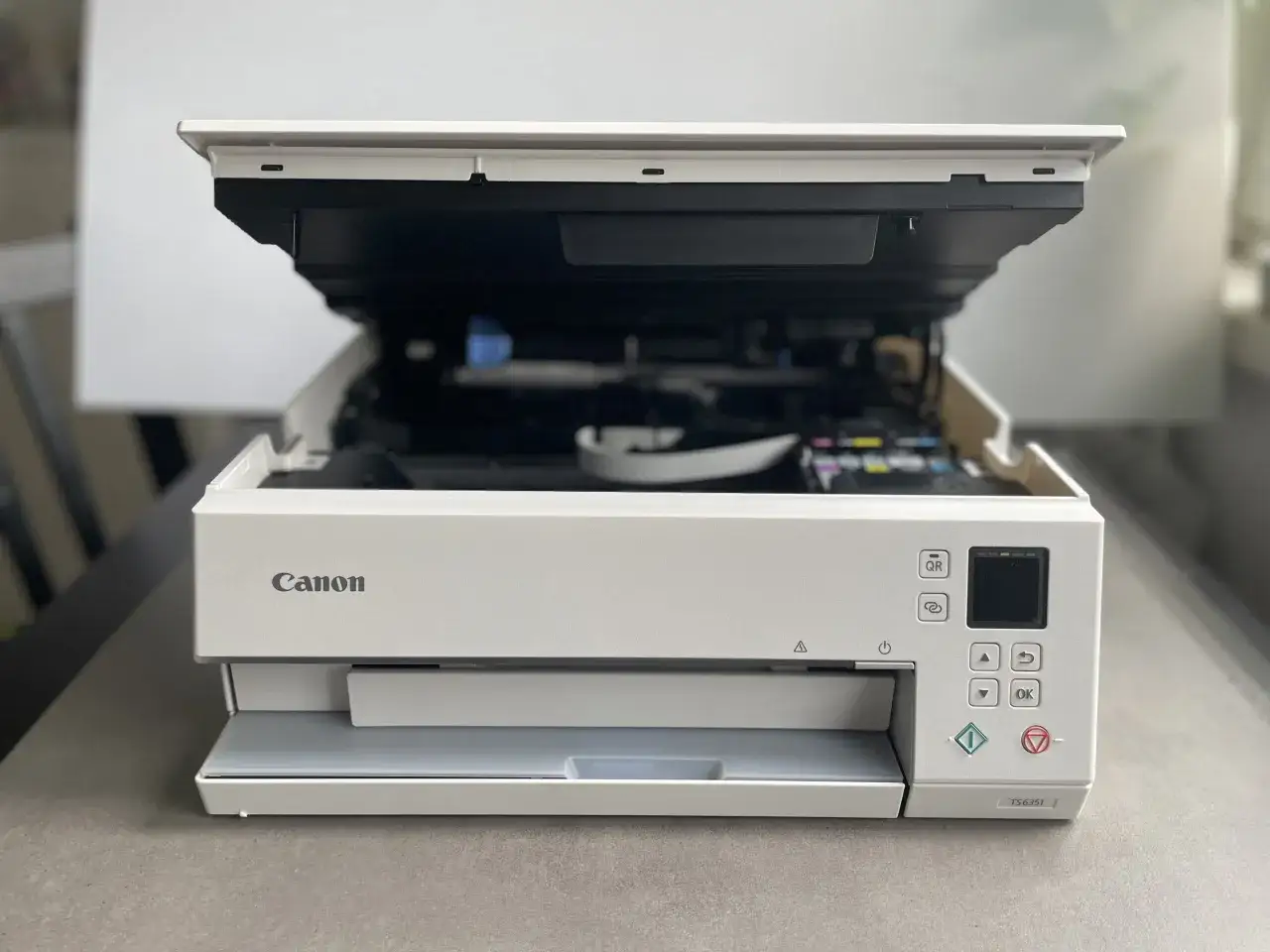 Biała drukarka Canon z otwartą pokrywą, widoczne tusze. Poradnik jak zainstalować drukarkę Canon.
